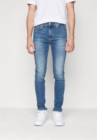 Ljusblå skinny jeans i denim med en urtvättad design, fem fickor och knappstängning. Bärs med vita sneakers.