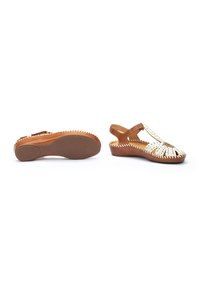 Chaussures slingback en cuir marron avec un motif découpé crème, semelle en caoutchouc texturé et surpiqûres décoratives le long des bords.