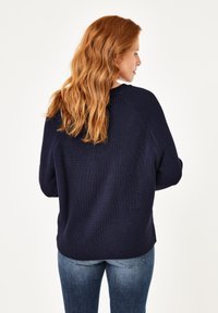 Marineblauer Strickpullover mit einer strukturierten Oberfläche, ausgestattet mit Raglanärmeln und einem gerundeten Saum, kombiniert mit blauen Jeans.
