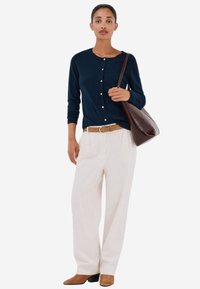 Laivastonsininen neulecardigan nappien kanssa, vaaleanbeige korkeavyötäröiset housut, ruskea vyö ja ruskeat korolliset nilkkurit, yhdistettynä ruskeaan olkalaukkuun.