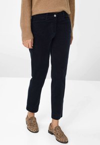 Marineblauwe corduroy broek met een rechte snit, voorzien van zilveren knoopdetails en zijzakken; gecombineerd met schoenen met luipaardprint.