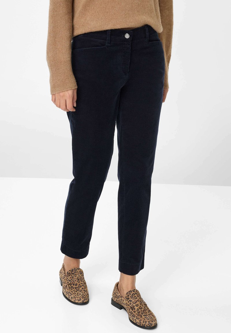 Marineblauwe corduroy broek met een rechte snit, voorzien van zilveren knoopdetails en zijzakken; gecombineerd met schoenen met luipaardprint.