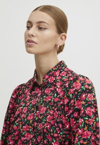 Blusa floreale con sfondo nero e vivaci motivi floreali rosa e verdi, con bottoni, colletto classico e texture di tessuto morbido.