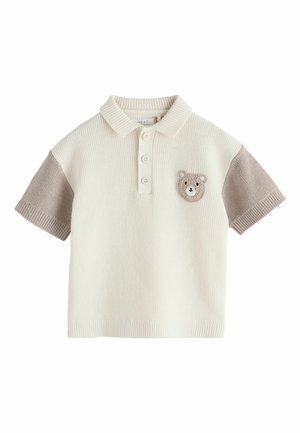 Kreemikas kootud polosärk beežide lühikeste varrukatega ja vasakul rinnal väikese heegeldatud karu näo plaastriga.