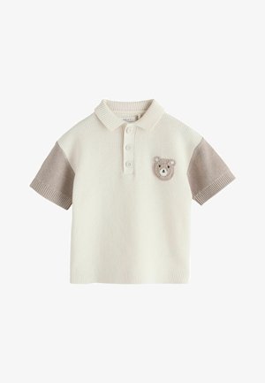 Tricou polo crem tricotat, cu mâneci scurte bej și o mică aplicație croșetată cu fața unui ursuleț pe pieptul stâng.