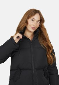 Giacca a vento nera con colletto alto, chiusura con zip e coulisse regolabile. Presenta tasche laterali e una texture trapuntata.