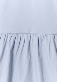 Hellblauer Stoff mit einer glatten Textur, der an dem Saum einen gerafften Volant aufweist. Der Stoff wirkt leicht und luftig.