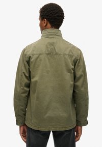 Veste olive en coton avec un design structuré, présentant un col montant et des détails de boutons au niveau des poignets.