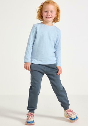 Camicia a maniche lunghe blu chiaro, pantaloni jogger grigi e sneakers multicolori con lacci rosa. Acconciatura carina con un accessorio per capelli rosa.