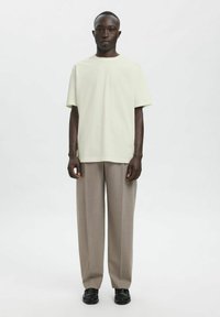 Lysegrøn kortærmet T-shirt kombineret med lysebeige vide bukser og sorte sko, stående mod en neutral baggrund.