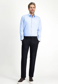 Lichtblauw overhemd met lange mouwen en knoopsluiting, gecombineerd met zwarte broek en donkere instappers. Gladde stof en een getailleerde pasvorm.