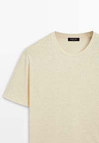 Jasnobeżowy bawełniany T-shirt z okrągłym dekoltem i krótkimi rękawami. Gładka faktura, minimalistyczny design, brak widocznych wzorów i zdobień.