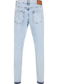 Jeans en denim bleu clair avec une coupe slim, présentant des poches arrière, une texture délavée et une étiquette de ceinture en cuir marron.