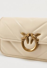 Κρεμώδης, κεντημένος δερμάτινος τσάντα χεριού με χρυσό μεταλλικό κούμπωμα σε σχήμα δακτυλίου, που απεικονίζει δύο πουλιά να ακουμπούν τα ράμφη τους.