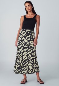 Musta maxihame, jossa on kermahdollinen abstrakti kuvio, valmistettu kevyestä kankaasta. Yhdistetty mustan istuvan hihattoman topin ja mustien sandaalien kanssa.