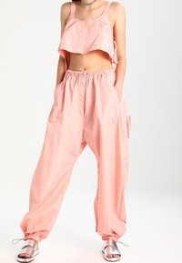 Lichtroze cropped top met gelaagd ontwerp,Pair met bijpassende lichte, baggy broek met elastische tailleband en zakken. Zilveren sandalen.