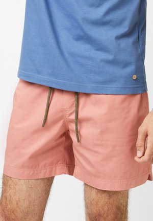 Shorts de bain roses avec une taille élastique et des cordons de serrage verts ; associés à un t-shirt en coton bleu à col rond.