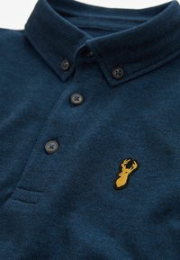 Mörkblå knapp-bak polo skjorta med en gul broderad älghuvud-logo på bröstet.