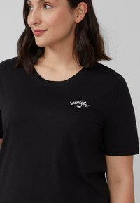 Zwarte t-shirt met korte mouwen, gemaakt van zacht materiaal, met geborduurde witte tekst "beautiful" nabij de halslijn. Ronde halsontwerp.