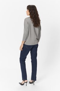Grå strikket sweater med en afslappet pasform og trekvartærmer, parret med mørkeblå jeans og sorte højhælede sko.