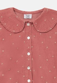 Rosa Corduroy-Hemd mit Rundkragen, verziert mit kleinen herzförmigen Dekorationen und weißen Knöpfen entlang der vorderen Leiste.