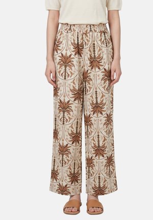 Pantaloni beige larghi con motivi di palme marroni, indossati con sandali marroni aperti e top crema a maniche corte.