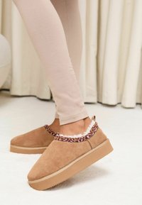 Pantofi slip-on din piele întoarsă de culoare cămilă, cu margine imprimeu leopard mov și căptușeală moale din blană, având o talpă groasă de cauciuc pentru confort.