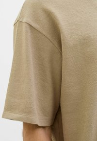 Beige kortærmet t-shirt med et struktureret, strikstof. Har en afslappet pasform og en rund halsudskæring. Søm-detaljer er synlige på skuldrene.