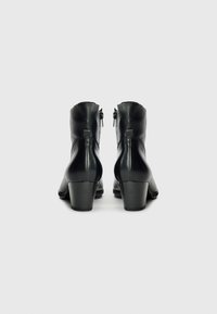 Bottines en cuir noir avec un talon carré, fermeture éclair et texture lisse, arborant un design épuré et minimaliste.