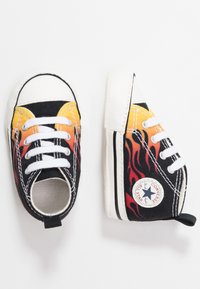 Czarne płócienne trampki z płomieniami w odcieniach pomarańczowym i czerwonym, białe sznurówki oraz gumowy czubek. Zawierają okrągłą naszywkę z logo Converse.