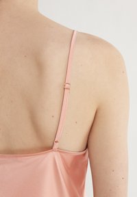 Satin rosa chemisett med tunna justerbara axelband, med en guldfärgad spänne bak och en jämn, glänsande yta.