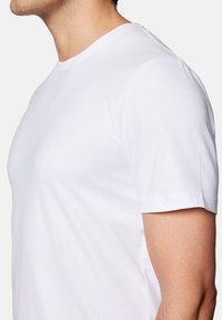 Biała koszulka z bawełny z krótkim rękawem, o dekolcie w serek, gładkiej fakturze i dopasowanym kroju, prezentująca widok z boku.