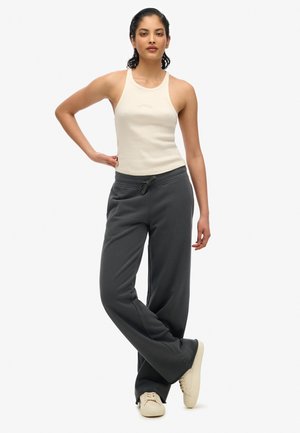 Beige geribbelde tanktop gecombineerd met losse grijze sweatpants, voorzien van een verstelbare tailleband en crèmekleurige sneakers. Eenvoudig en ontspannen ontwerp.