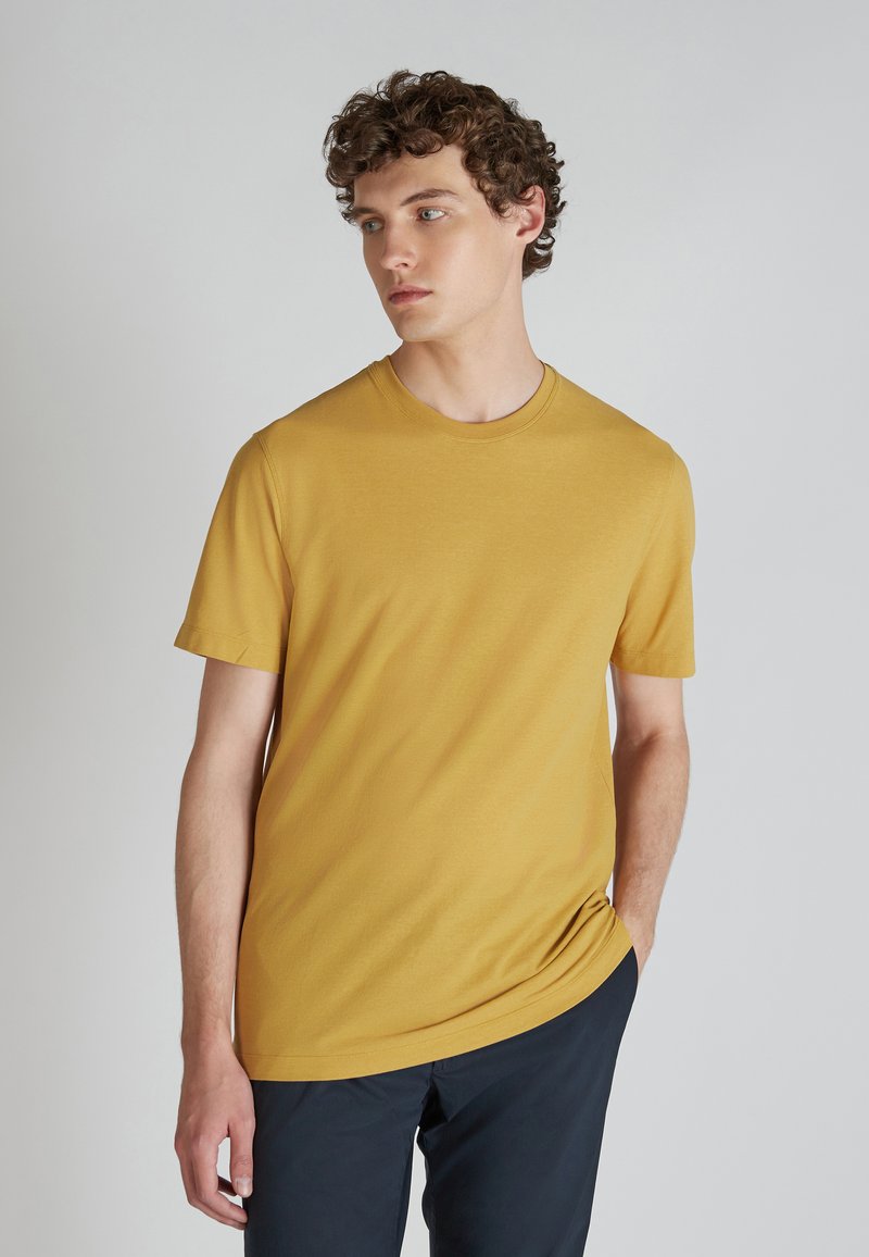 T-shirt a maniche corte, collo rotondo in cotone giallo senape. La vestibilità è rilassata con una texture liscia e senza motivi visibili.