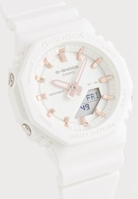 Valge G-Shock käekell kuue nurga kujuga korpusega, roosakullatud detailide, digitaalse näidiku ja tekstuuriga silikoonist rihmaga. Veekindel, tähistatud WR20BAR.
