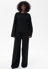 Czarny sweter z dzianiny z długimi rękawami oraz szerokie, luźne czarne spodnie. Oba elementy charakteryzują się miękką teksturą i minimalistycznym wzornictwem.
