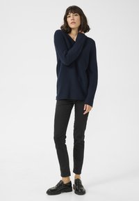 Marine-blau gestreifter Pullover mit weitem Ausschnitt, kombiniert mit schwarzen Slim-Fit-Hosen und schwarzen Slippers. Glatte Textur, lässiges Design.