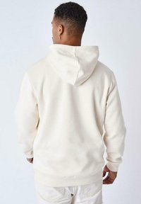 Sudadera crema con capucha ajustable, puños y cintura de canalé. Textura suave, corte relajado y diseño minimalista.
