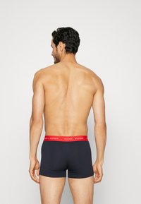 Temno modre bokserice iz bombaža z rdečim elastičnim pasom, na katerem je napis "TOMMY HILFIGER". Gladka tekstura in oprijet dizajn.