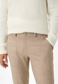 Beige gemusterde broek met een knopen sluiting en zijzakken, gecombineerd met een textuurcrème trui met ribgebreide manchetten en strepen.
