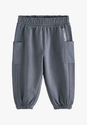 Arm ruht in der Seitentasche von grauen Jogginghosen mit elastischem Bund und weißem "ALLSAINTS"-Schriftzug am Taschenrand.