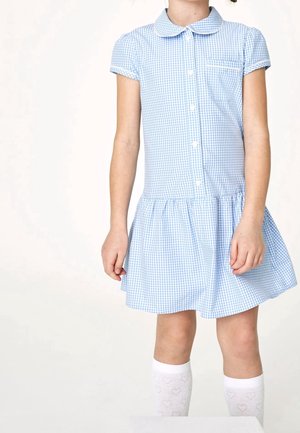 Child wearing a light blue and white checkered dress with buttons and white knee-high socks with heart patterns, standing against a plain background.