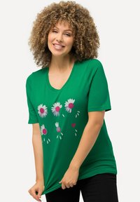 Camiseta de algodón verde con escote en V, que presenta estampados florales en blanco y rosa, con acentos de pequeños corazones y hojas. Mangas cortas.
