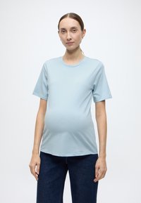 Γαλάζιο κοντομάνικο τοπ εγκυμοσύνης από απαλό ύφασμα, με στρογγυλή λαιμόκοψη και άνετη εφαρμογή, σε συνδυασμό με σκούρο τζιν παντελόνι.