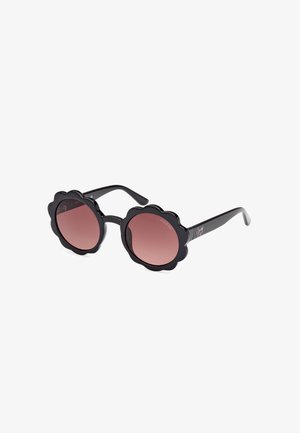 Schwarze, blumenförmige Sonnenbrille mit einem Farbverlauf in Rosé. Verfügt über dicke Kunststoffrahmen und schlanke schwarze Bügel. Markenname ist auf dem Glas angebracht.