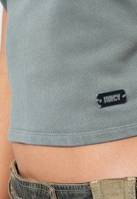 Mintegodra kratka majica iz mehkih materialov z srebrnim logotipom "JUICY" in klasičnimi šivi na robu.