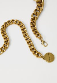 Kultaävyinen ketjun kaulakoru, jossa on suuria lenkkejä ja pyöreä tagi, jossa on kaiverrettuna "MICHAEL KORS". Varustettu hummerilukolla kiinnittämistä varten.