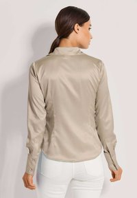 Beige Satin-Hemd mit langen Ärmeln, Kragen, abgerundetem Saum und geknöpften Manschetten. Glatte Textur, taillierte Passform und minimalistischer Stil.