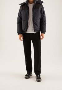 Mørkeblå dunjakke med lynlås foran og elastiske mansjetter, parret med sorte bukser og grå sportsko. Casual, lagdelt design.