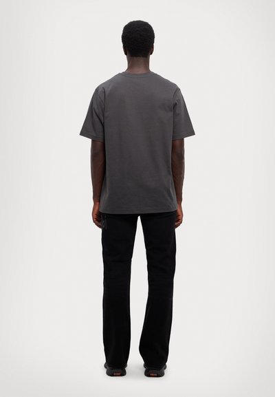 T-shirt en coton gris foncé avec une coupe décontractée et des manches courtes, associé à un pantalon noir. Le tissu semble lisse et confortable.